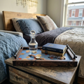 A rustic wooden nightstand in a bedroom setting, styled with a matching wooden tray, a glass decanter, a stack of books, and a watch.